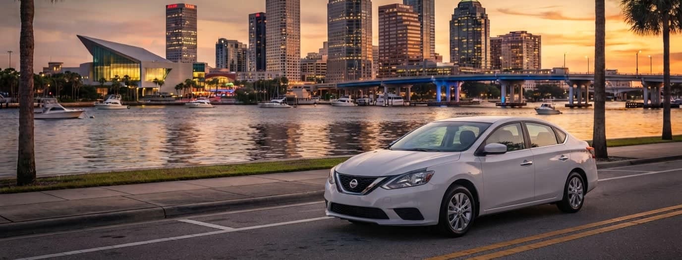 A white saloon parked on Bayshore Boulevard at sunset, with the downtown Tampa skyline across the water